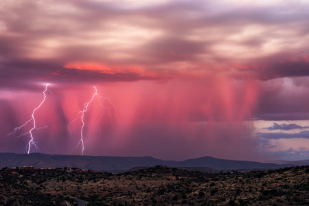 Lightning strikes in the sky during a thunderstorm at sunset.