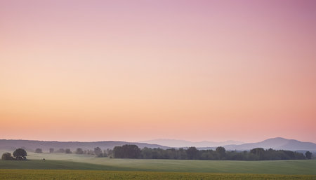 Sunset over a meadow with trees and hills in the backgroundの素材