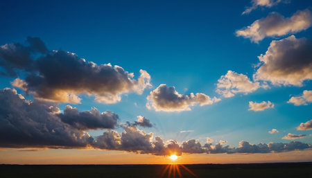 Sunset over a field with green grass and blue sky with cloudsの素材