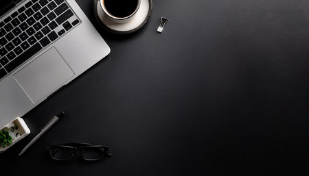 Black office desk table with laptop, coffee cup and glasses. Top view with copy spaceの素材