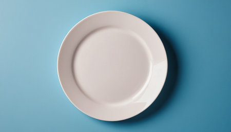 Empty white plate on blue background. Top view, flat lay.の素材
