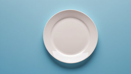 Empty white plate on blue background. Top view with copy space.の素材