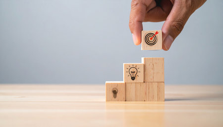 Businessman hand holding wooden cube with light bulb icon on top of wooden table.の素材