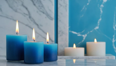 Three burning candles on a marble countertop against a blue marble wallの素材