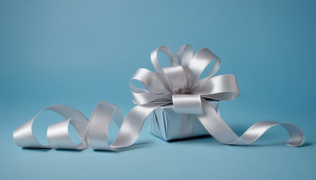 Gift box with silver ribbon bow on blue background, copy spaceの素材
