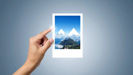 Hands holding photo frame with mountains on blue background, travel conceptの素材