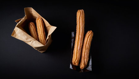 Churros in a paper bag on a black background. Top view.の素材