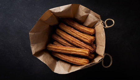 Churros in a paper bag on a black background. Toned.の素材