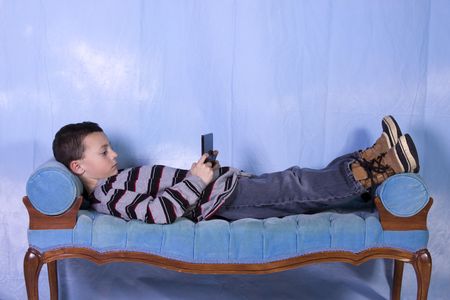 Little Boy Playing Handheld Video Game on the Couchの写真素材