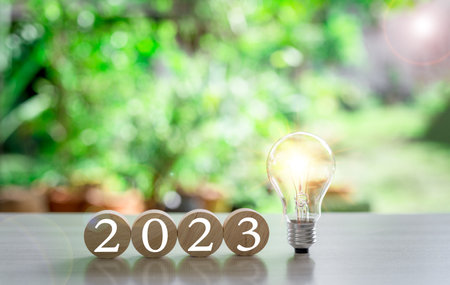 The new year 2023 and bright light bulb on table. Concept of a startup that drives economy, finance,...