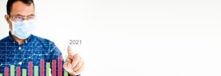 Closeup, Businessman wearing a coronavirus face mask, or COVID-19, is pointing his finger at a color graph showing market activity 2021. Copyspace on the right for a design blurred white background.の写真素材