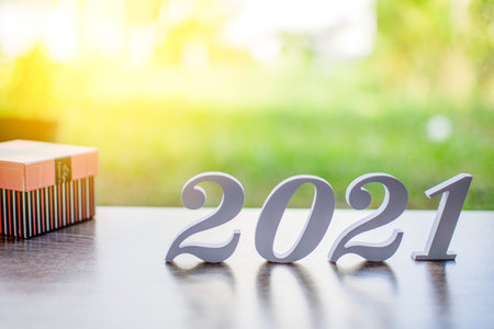 The daylight, Happy New year 2021, Closeup the white letters 2021 and Italic and gift on wooden table and copy space on top for input design and text, Starting of New year concept. Blurred backgroundの写真素材