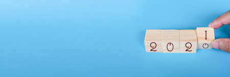 Wooden cube with word 2020 to 2021 New Year concept on blue background. Close-up and copy space on left for design or text. A man's hand holding a cube that is changing the year 2021.の写真素材