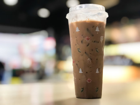 Close-up, iced coffee on a wooden table in the shop. Coffee cup with christmas icon. Copy space on right for design or text. Blurred background.の写真素材