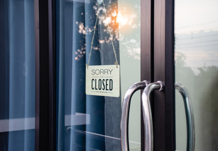 The board hung in front of the glass door of the coffee shop had a message sorry and closed. Light from the soft sun in the morning was bright as the background. Reflection from nature, sky, treesの写真素材