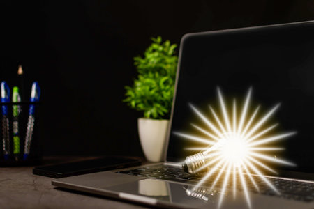 Close-up. A bright light bulb on a laptop. Concept of start-up that drives economy, finance, banking, real estate. Bright lights give hope to businessmen both small and large. Blurred black backgroundの写真素材