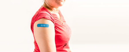 A blue plaster is attached to the woman's arm. Concept for first aid after coronavirus (COVID-19)...