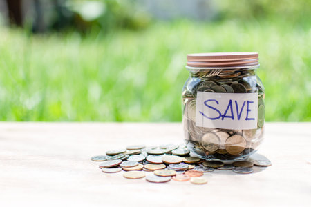 Blurred background, Coins and text SAVE in a glass jar placed on a wooden table. Concept of saving...