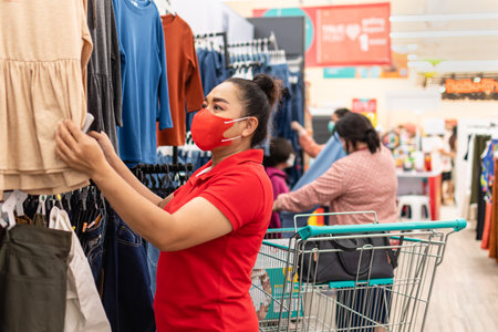Close-up, Woman wearing mask who chose clothes for her special day In Women's apparel department of a supermarket on a casual day, Concept for shopping,  lifestyle, selective focus, blurred backgroundの写真素材