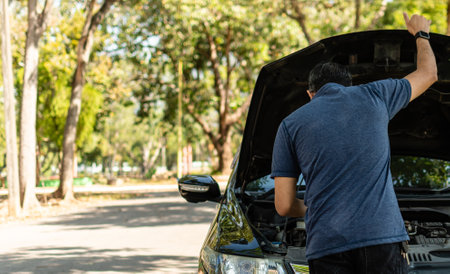 Man stands and inspects a broken-down car in a rural suburban forest. Black car, Engine won't start....