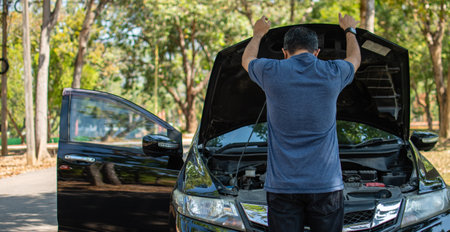 Man stands and inspects a broken-down car in a rural suburban forest. Black car, Engine won't start....