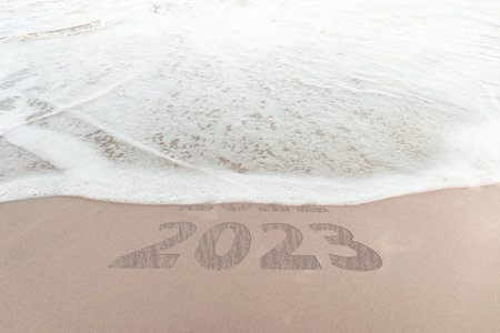 change new year of 2023 on sand of beach. New Year 2023 Concept. inscription is a 2023 number on sand beach. Sandy beach and sea wave beautiful background. Write letters by hand on the beach.の写真素材