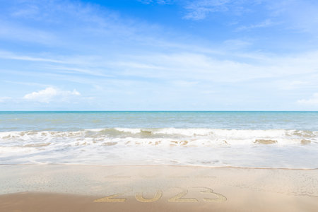 New Year 2023 Concept. inscription is a 2023 number on sand beach. Sandy beach and sea wave...