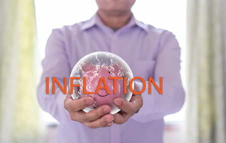 A Businessman holding a pink piggy bank in severe inflation situations around the world. Concept, finance, banking, interest rates, economy. Selective focus, Closeup, Blurred backgroundの写真素材