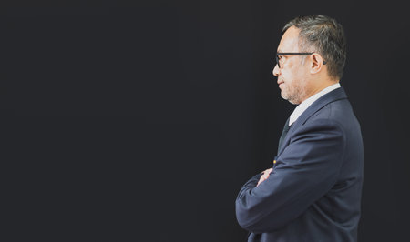 A businessman in a black suit stands facing forward and looks forward. Smart Standing Man, Doing Business Broker, Manager, Accountant, Bank Clerk Concept. closeup, copy space on left. black backgroundの写真素材