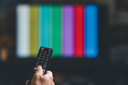 Hand holding TV remote control in front of tv screen with colorful background
