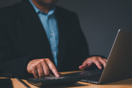 Businessman typed on a laptop computer, fingers flying over the keyboard as he calculated financial reports for company. His eyes were focused on a screen, and face was serious as he workedの写真素材