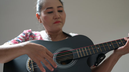 Woman passionately plays acoustic guitar, hands expertly fret colorful strings. Music fills quiet space, expressing creativity. Female musician enjoys practicing musical instrument, developing skill.の写真素材