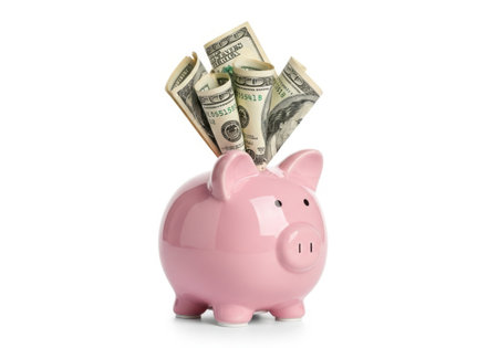 A pink ceramic piggy bank overflowing with US dollar bills, presented isolated on a clean white background.の素材