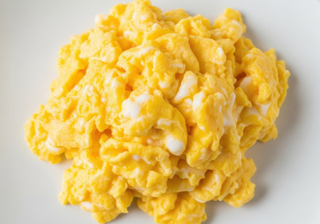 A close-up, overhead view of a pile of fluffy, yellow scrambled eggs, presented isolated on a clean cream beige background.の素材