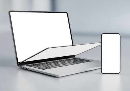A modern laptop and a smartphone are displayed side-by-side with their screens blank, isolated on a clean light gray background.の素材