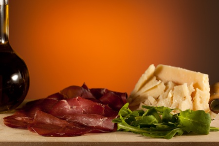 Sliced bresaola ham with salad and parmesan cheese with an oil bottle, over a wooden chunk-boardの写真素材