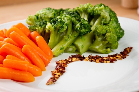 Steamed broccoli and baby carrots with red pepper in a white dishの写真素材