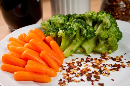 Boiled broccoli and baby carrots with red pepper in a white dishの写真素材