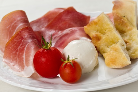 Dish with typical Italian food. Raw ham, mozzarella cheese, cherry tomatoes and focaccia pizzaの写真素材