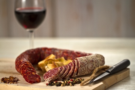 Salami and spicy salami with focaccia pizza decorated with  peppergrain and grounded red pepper over a wooden chunk-board. With a red wine glass on backgroundの写真素材