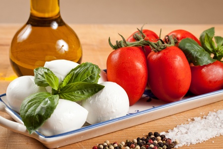 Mozzarella cheese bits and cherry tomatoes with basil leaf. Healty caprese salad with oil bottle, salt and pepperの写真素材