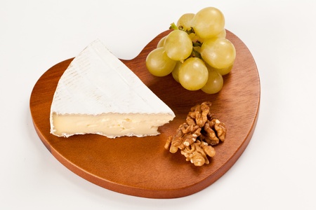 Piece of Brie french cheese with grapes and nuts over an hearth shaped wooden board in isolated studio shotの写真素材