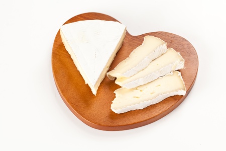 Piece and slices of  franch brie cheese over an heart shaped wood board in isolated studio shotの写真素材