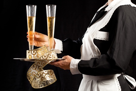 Young waitress in uniform serving two glasses of champagne with tray and festive gold decorationsの写真素材