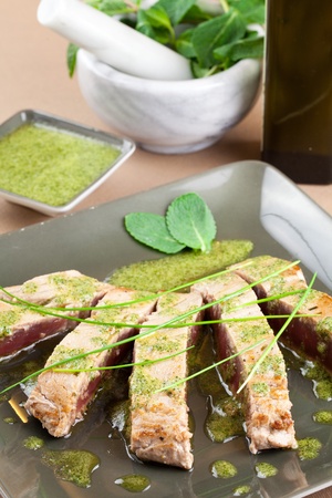 Delicious tuna steak with mint sauce. Sliced and decorated with chive and mint leafs. Served in a trendy green dishwareの写真素材