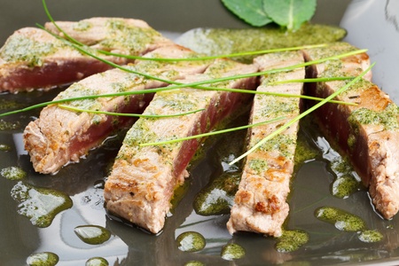 Delicious tuna steak with mint sauce. Sliced and decorated with chive and mint leafs. Served in a trendy green dishwareの写真素材