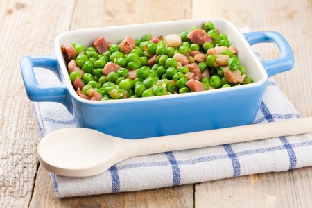 Terrine of peas cooked with bacon and ham over a rustic napkin and a wooden tableの写真素材