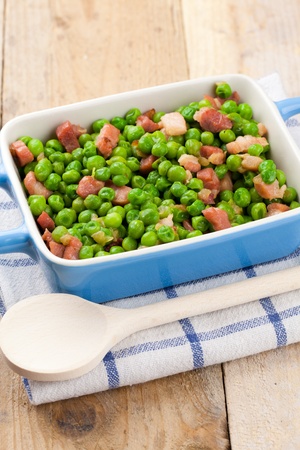 Terrine of peas cooked with bacon and ham over a rustic napkin and a wooden tableの写真素材