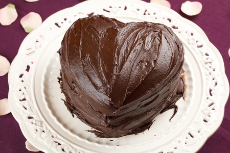 heart shaped chocolate cake in a traditional dish over a purple table cloth decorated with rose petalsの写真素材