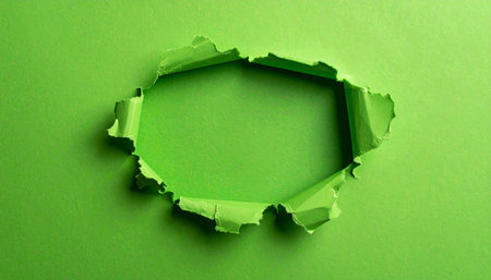 A rough, irregularly shaped hole is torn through a smooth, flat green paper surface.の素材